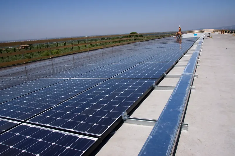 Photovoltaikmodule auf einem Flachdach, im Hintergrund Monteure bei der Arbeit